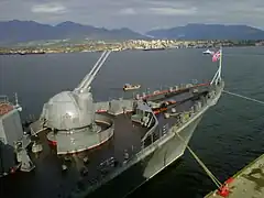 Una vista cercana de los cañones de doble propósito AK-130 en la proa con la costa norte de Vancouver al fondo.