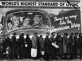 Demandantes de ayuda de emergencia, todos ellos negros, alineados irónicamente ante un anuncio en el que una feliz familia blanca en automóvil representa el "mayor nivel de vida del mundo - No hay forma de vida [way también significa "carretera"] como la forma de vida americana, 1937.