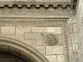 Escudo decorativo y motivo de espada en la enjuta del arco, con inscripción encima.