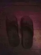 Chanclas de color café oscuro, sobre un piso de tablas de madera, también café.