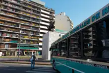 Vista del monumento al Cid Campeador. Se aprecia una persona cruzando por la senda peatonal mientras el colectivo de la línea 92 espera para doblar por la Av. Dr. Honorio Pueyrredón