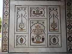 Floreros de pietra dura en el muro de mármol con bordura floral geométrica.
