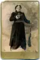 Una postal de 1910 (frente), la cual retrata la viuda de Kevork Chavush, Heghine. En la parte frontal de la postal, se puede ver la imagen en blanco y negro de una mujer con un vestido largo y negro; Ella sostiene una pistola en su mano derecha y un rifle en la izquierda. Las bandoleras están envueltas alrededor de su torso y cintura. Casi invisible entre las balas y el cuero se ve un broche redondo o medallón sobre su pecho izquierdo.