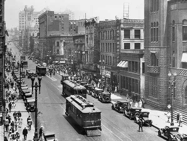 Mirando hacia el norte a lo largo de Broadway, y su lado oriental en el año 1924. Arriba a la izquierda, el antiguo edificio Los Angeles Times estilo castillo, y detrás el antiguo Registro Público (Hall of Records). El edificio Cámara de Comercio, Broadway no. 128. Farmacia en el edificio Hellman (no. 144–6) esquina noreste de la Calle 2ª. Dentista en el edicificio Nolan, Smith and Bridge Bldg. (no. 200–4), esquina sureste de la 2ª. Hotel ¨New King Hotel¨ en el edificio Gordon (no. 206–10). Victor Clothing donde estaba ubicado del 1926 al 1964 en el edificio Crocker (no. 212–6). Restaurante y dulcería ¨Pig 'n Whistle¨ en el edificio Copp (no. 218–224). El Palacio Municipal del año 1888 se ve al extremo derecho.