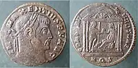 Follis de bronce acuñado por Majencio en Roma en 308 - 310. Esta moneda conmemora la reconstrucción del templo de Roma tras el incendio en 307. En el reverso aparece Roma sosteniendo el orbe y el cetro, entregándoselo al emperador que tiene un cautivo. Se le ve sentado dentro de un templo hexástilo con un escudo en el suelo.