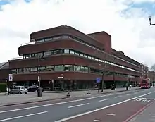 Exterior del gran edificio de ladrillo y vidrio rojo de tres pisos al lado de la carretera.
