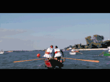 Mujeres que reman en barco rojo, en la laguna de Venecia. Día soleado. Mujeres vestidas con una camiseta blanca y una minifalda blanca.