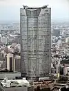 Aerial view of a gray, oval-shaped high-rise lined with rows of windows; the facade is bisected by a smaller mid-section
