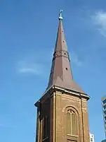 Detalles de la torre y aguja mostrando su forma octagonal. En esta vista el cobre ha sido renovado y se ve café y brillante. Encima están una cruz y bola con pátina verde. La torre es de tabique, tiene pilastras de esquinas cortadas y lumbreras largas en la ventana