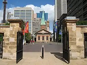 Una foto reciente. La iglesia se ve bordeada por los postes de las puertas de los cuarteles. El campanario se puede ver contra el contexto de edificios de varios pisos