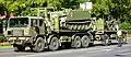 Iveco-Pegaso M.320.42WM 8×8 VEMPAR táctico transportando un M-113VCZ sobre la plataforma y una minimáquina cargadora Bobcat en el remolque.