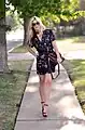 Mujer con vestido estampado corto caminando en la acera con bolso.