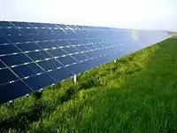 Los paneles solares, con un ángulo de unos 30 grados, reflejan el cielo azul por encima de un campo cubierto de hierba.